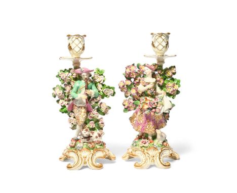 A pair of Chelsea candlestick figures, c.1765, of a shepherdess and her companion, each standing before flowering spring boca