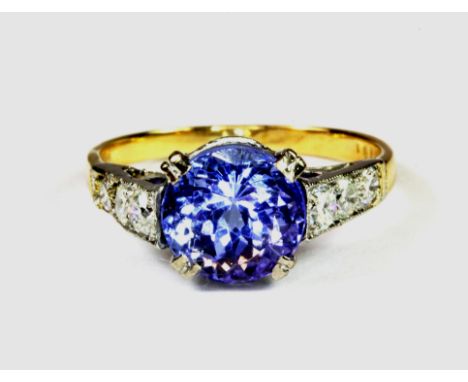 A yellow and white gold (stamped 18ct) ring set with a lovely round cut tanzanite and diamond set shoulders, (K.5).