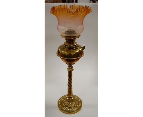 A late Victorian oil lamp having amber tinted frilled etched glass shade above a brass font on a spirally turned column and c