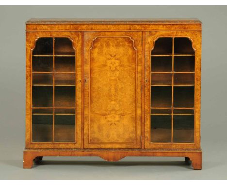 A walnut veneered display cabinet, with foliate carved cornice above a centre panelled door flanked on either side by a glaze