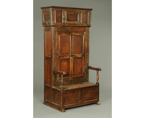 A 19th century oak panelled bacon settle, with two cupboards above a box seat with lift up compartment, with panelled front a