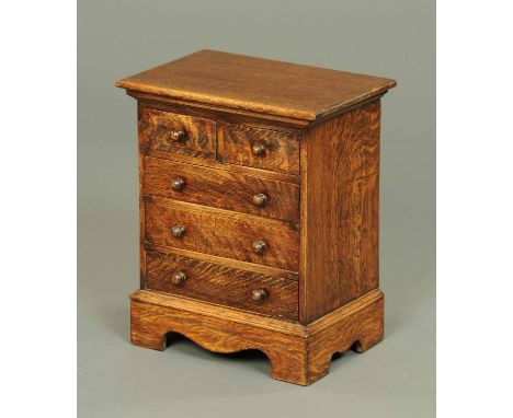 A Victorian style oak miniature chest of drawers, with two short and three long graduated drawers and raised on bracket feet.