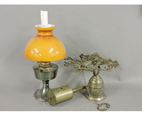 An early 20th century oil lamp, with glass shade, a brass bell, and a brass clockwork bottle jack