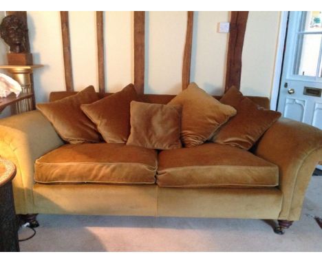 A large gold velvet upholstered sofa, with roll over arms and feather filled cushions, standing on turned feet and castors, 2