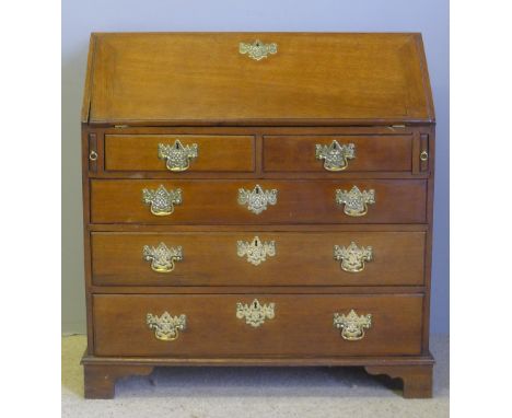 A George III oak bureauThe rectangular top above the fall with pierced brass escutcheon, enclosing the fitted interior, over 