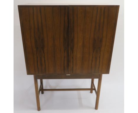 A MID CENTURY ROSEWOOD COCKTAIL CABINET, the two doors fitted for glasses, two drawers, twelve bottle holders and shelves, on