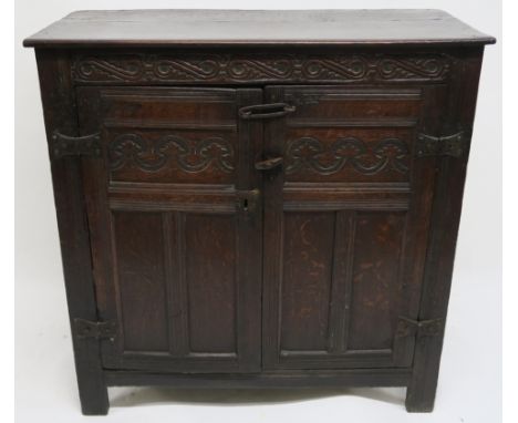 A 17TH CENTURY DESIGN OAK LIVERY CUPBOARD carved with a scroll frieze above a pair of panelled doors, enclosing a shelf, 118c