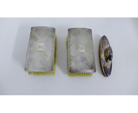 A pair of Birmingham silver backed clothes brushes, each with engine turned decoration, together with a silver backed nail bu