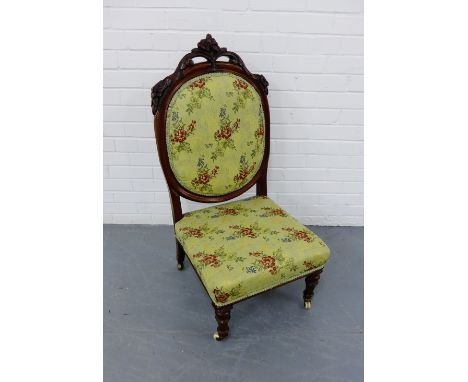 A late Victorian mahogany framed nursing chair having a carved top rail over padded back support and stuff over seat upholste