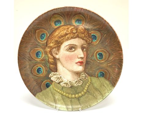 A large earthenware pottery charger with hand painted view of a lady using peacock feathers. Named and dated to reverse 1884 