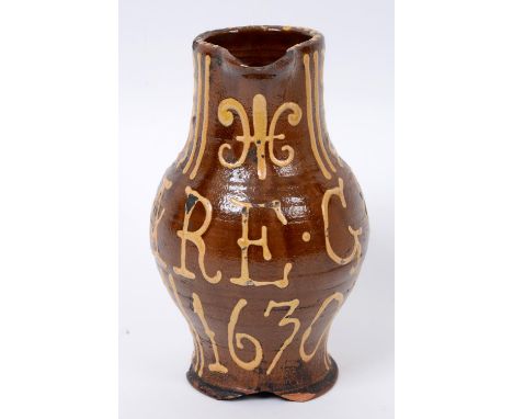 A 17th century slipware jug, with fleur-de-lys style motif and linear decoration, bears motto FEARE GOD 1630, 18.5 cm high  S