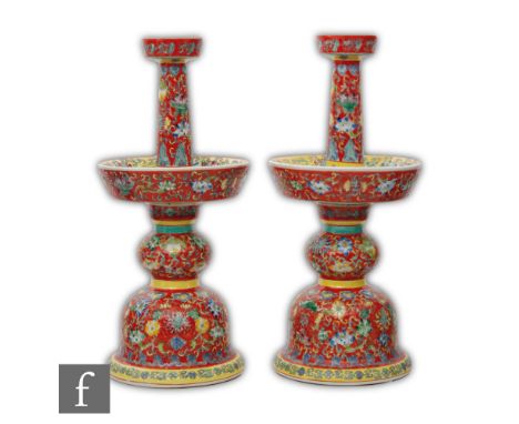 A pair of Chinese famille rose porcelain candlesticks, rising from a bell-shaped base with two-tiered drip pans, the knopped 