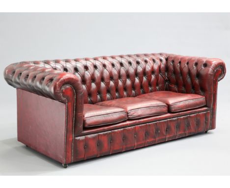 AN OX-BLOOD LEATHER THREE-SEATER CHESTERFIELD SOFA, with deep-buttoned back and arms, moving on castors. 188cm long