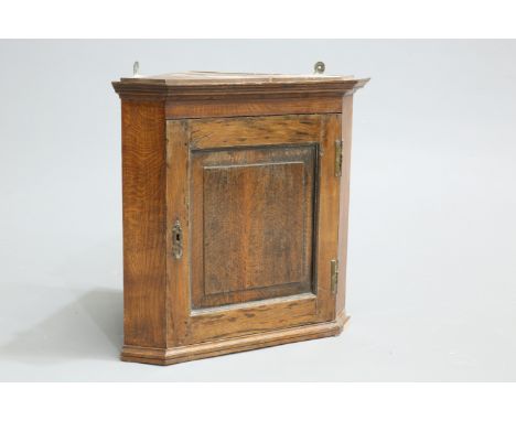 A SMALL GEORGE III OAK HANGING CORNER CUPBOARD, with fielded panel door. 55cm high, 59.5cm wide