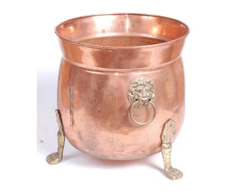 An early 20th century copper and brass jardiniere, flanked by brass lion mask ring handles, standing on three paw feet, h.26c