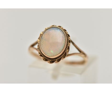 A 9CT GOLD OPAL RING, oval cut opal cabochon, collet set with a fine rope twist surround, bifurcated shoulders leading onto a