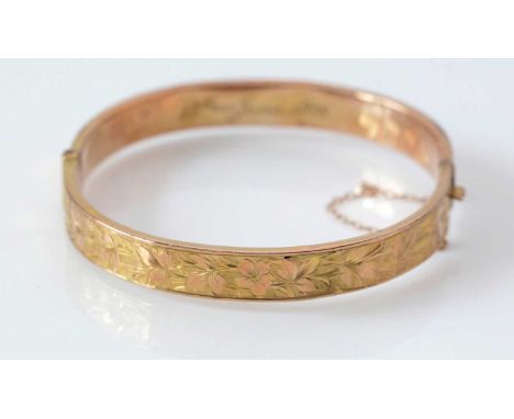 A 9ct. yellow gold bangle, half engraved with floral decoration, 7.7grms.