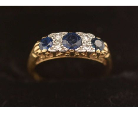 A sapphire and diamond ring, the three circular-cut sapphires parted by brilliant-cut diamonds, in Victorian style scrolling 