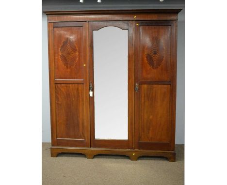 An Edwardian three-door mahogany and inlaid wardrobe, the projecting cornice above a central shaped mirror plate flanked by a