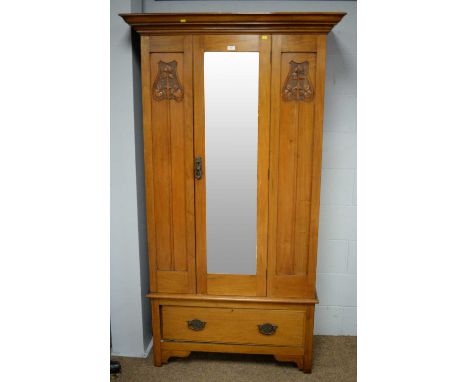 An Art Nouveau style walnut wardrobe, the projecting cornice above a single bevelled mirror plate door, flanked by stylized f