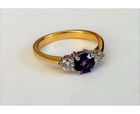 An 18ct gold, amethyst and diamond set three stone ring, claw set with the circular cut amethyst to the centre, between two s