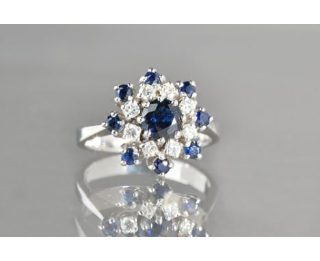 A white gold, sapphire and diamond set shaped circular cluster ring, claw set with the principal circular cut sapphire to the