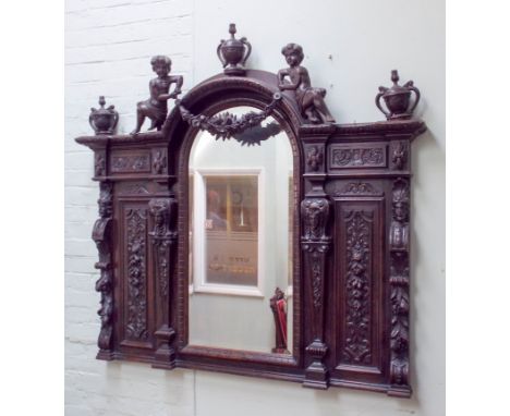 A Victorian heavily carved, dark oak, over mantel mirror, decorated with cherubs, masks and floral carvings, mounted with thr