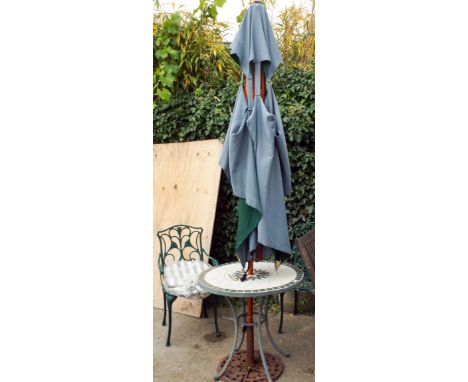 A circular tile top patio table with two green painted elbow chairs with cushions and a parasol with iron base 
