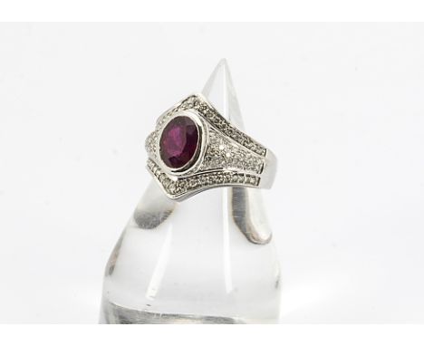 A contemporary 18ct white gold ruby and diamond dress ring, the oval mixed cut ruby in collet setting surrounded by brilliant