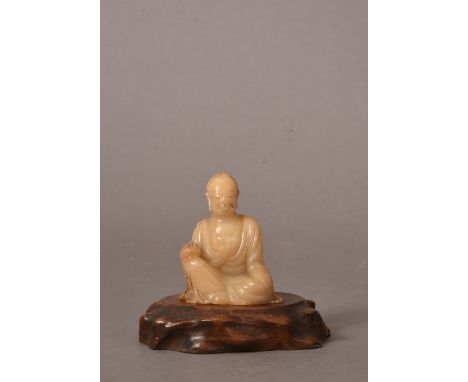 C17th Chinese soapstone figure of a Luohan, shown seated and holding a scroll above his raised right leg, wearing long robes 