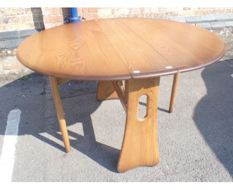 AN ERCOL STAINED ELM OVAL DROP-LEAF DINING TABLE paper labelled design 1156, and with button label 107 x 122cm (open)