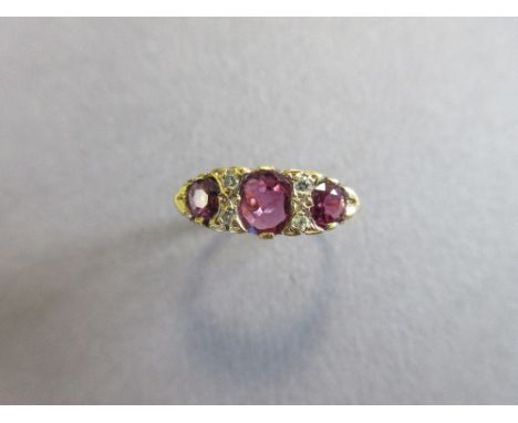 An Edwardian style 18ct gold ruby and diamond ring, with three graduated oval cut rubies separated by pairs of round brillian
