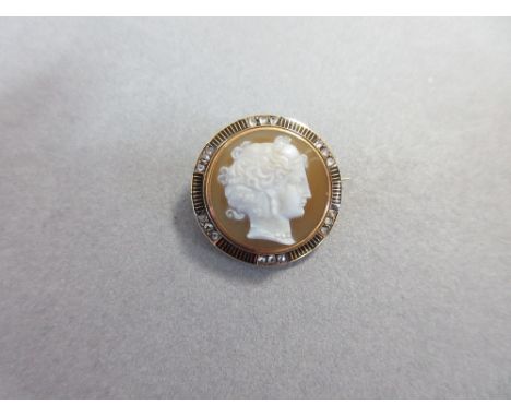 A hardstone cameo and diamond brooch, of circular form depicting the head of a young woman in profile with ornately dressed h