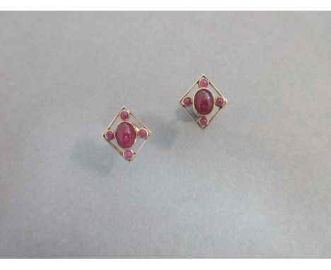 A pair of cabochon ruby earstuds, each earring of pierced diaper outline enclosing a collet set oval cabochon ruby with four 