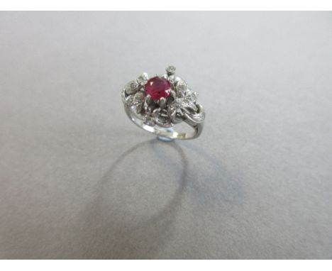 A ruby and diamond foliate knot ring, the central round cut ruby claw set in a pierced design of looped and knotted leafy ste