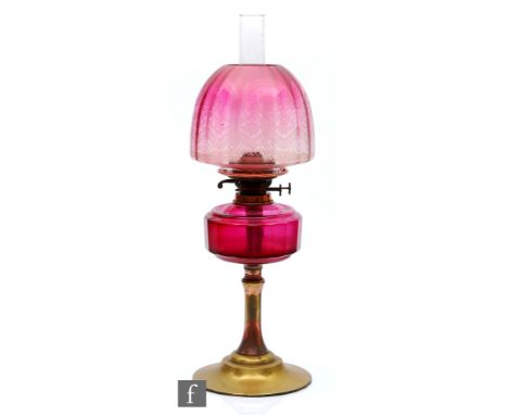 A late 19th Century oil lamp, the brass spreading circular base supporting a faceted cranberry glass reservoir, with floral a