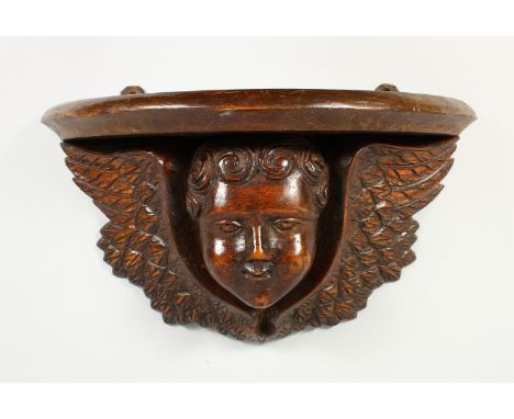 A WOODEN WALL BRACKET, carved as a winged cherub head. 13.5ins wide.