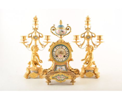 A 19th century French ormolu mantel clock and garnitures. Topped with painted ceramic loving cup, swags of flowers frame a pa