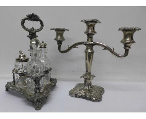 A plated three bottle cruet stand with three bottles, two with silver tops and an associated silver spoon, and a candelabra