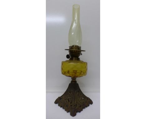 An oil lamp with cast metal base and amber glass reservoir