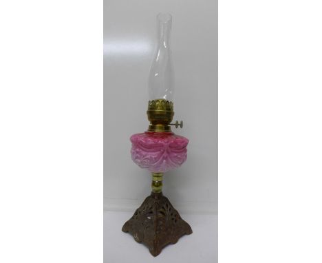 An oil lamp with cast metal base and pink glass reservoir