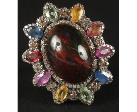 A LARGE DRESS RING set in white metal with cabochon galaxy black opal surrounded by multi coloured oval-cut sapphires and R/C