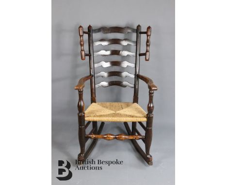 An oak ladder back rocking chair. The chair having a rush seat, on baluster legs, pad feet with rocker support.