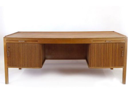 A 1960's oak and crossbanded desk with two slides and two tambour doors enclosing shelves, on square straight legs, designed 