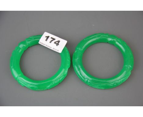 A pair of Chinese carved apple green jade/ hardstone bangles, carved with two dragons holding a pearl. Overall dia. 9cm, inte