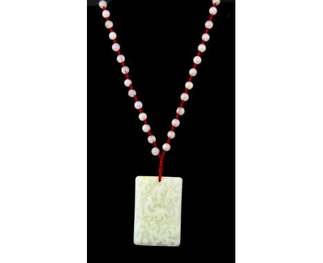 A Chinese carved mutton fat jade/ hardstone dragon amulet on a silk and rock crystal cord, H. 6.8 x 4.5 x 1cm.