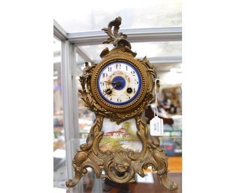 A 19th Century Rococo style gilt metal eight day mantle clock, the white dial with Arabic numerals, with a painted porcelain 