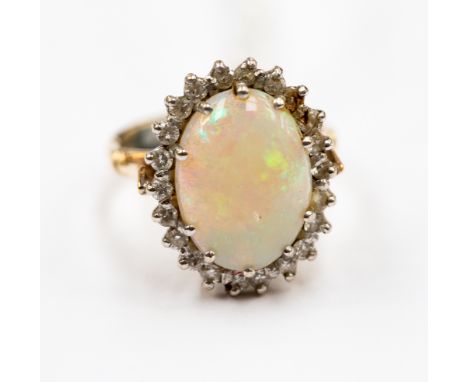 An opal and diamond cluster ring with oval cabachon displaying green and coloured fire within border of brilliant cut diamond