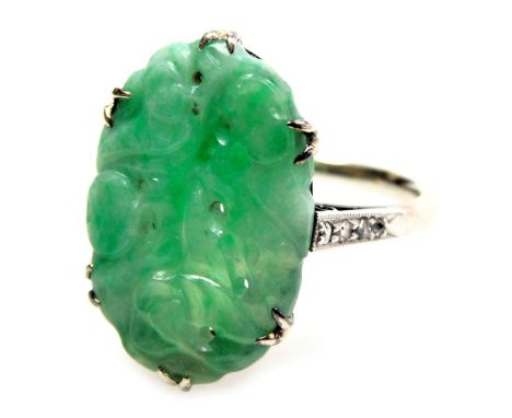 A jade ring, of oval carved sinuous form, in a claw setting, with diamond set shoulders, white metal, stamped 18 and Pt, size