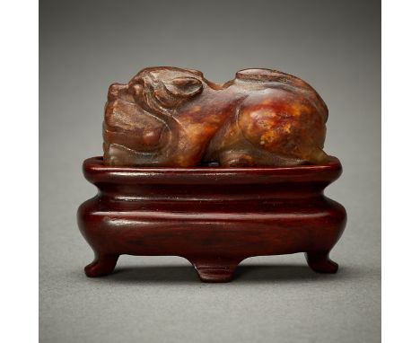 Chinese jade bead carving depicting a recumbent lion or mythical beast. Predominantly of an opaque honey-colored brown with r